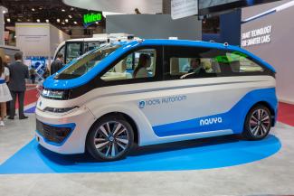 Photographie en couleur d’une voiture dans un salon de l’automobile. On peut lire sur la voiture 100 % autonom navya.