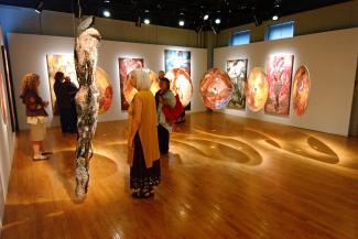 Six personnes dans une galerie d'art regardent des œuvres pendant qu'un puits de lumière éclaire la salle.