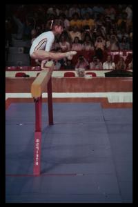 Photographie de la performance de Nadia Comaneci, en suspens sur la poutre.