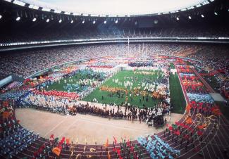 Photographie couleur du spectacle au stade olympique, avec une foule sur le terrain et la piste de course.