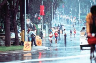 Photographie de deux athlètes courant sous la pluie dans le circuit de course qui passe par les rues.