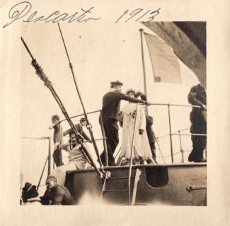Photo en noir et blanc montrant quelques personnes et un marin sur une partie extérieure d’un grand bateau.