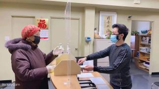 A young man and an elderly woman, both of Chinese origin, on either side of a counter in a spacious office.