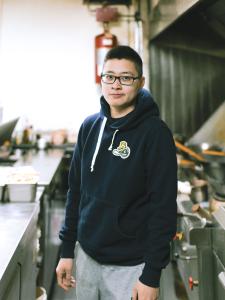 Colour photograph of a young man wearing glasses in a restaurant.