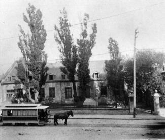 Vue sur le Château Ramezay bordé d'arbres, et sur la rue Notre-Dame avec un tramway tiré par un cheval.