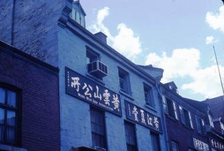 Gros plan sur le haut de façades de maisons du Quartier chinois. Sur celle du centre, deux enseignes en chinois, dont une sur laquelle on peut aussi lire Wong Wun Sun Association.