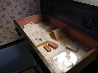 Vitrine qui se trouve dans un tiroir de commode dans une exposition avec différents artefacts dont des sachets de condoms des années 1950 et une trousse de prévention des maladies vénériennes et son livret d’instructions. 