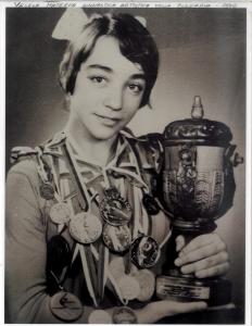 Photo noir et blanc d’une athlète de 16 ans en format taille avec plusieurs médailles autour du cou et un trophée qu’elle tient dans ses mains.
