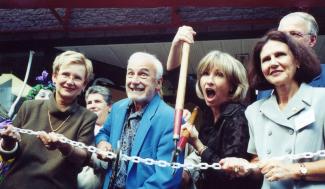 Trois femmes et un homme très souriants sont devant une chaîne et une femme coupe l’attache avec un immense ciseau.