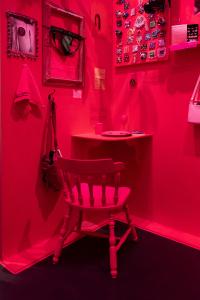 Le coin d’une pièce où tout est rose, les murs, la chaise, une tablette, sauf quelques objets sur les murs.