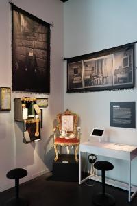 Photo montrant une section d’exposition dans le coin d’une pièce avec des bannières et panneaux au mur, différents objets dont un fauteuil et une table avec un iPad