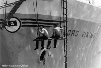 Photo de marins peignant la coque d’un bateau.