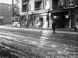 Photographie noir et blanc de la rue Wellington au premier plan et, en arrière-plan, du commerce Tousignant & Frères. Un policier se tient debout dans la rue sur la droite. 