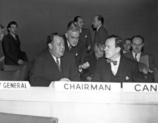 Deux hommes attablés dans une salle d’assemblée discutent.