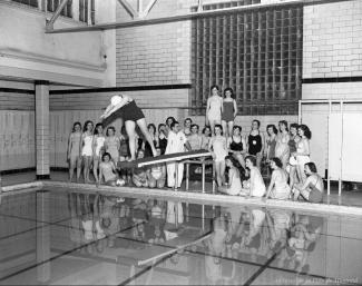 Reportage photographique sur un groupe de jeunes filles du High School au bain Lévesque. On y voit les jeunes filles dans la piscine et au plongeoir sur la présente photo.
