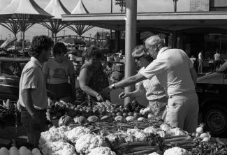 Des gens pointent des légumes autour d'un étal au marché.