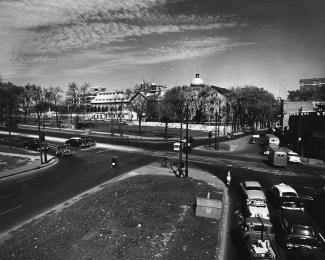 Photographie noir et blanc montrant une intersection routière. En bas à droite, il y a plusieurs voitures. Au-delà de l’intersection se trouve l’Hôtel-Dieu de Montréal. 