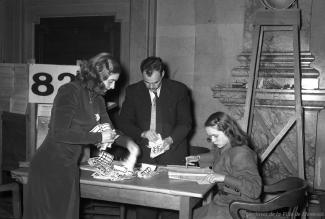 Photographie de trois personnes employées au dépouillement des votes du bureau de scrutin no 82 dans le hall d'honneur. 