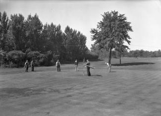 Photographie noir et blanc de six golfeurs sur un terrain. 