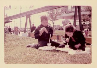 Deux enfants mangent un repas de casse-croûte assis sur la pelouse à Expo 67