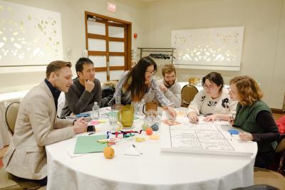 Six personnes travaillent sur une grande affiche blanche posée sur une table. Des crayons de couleur sont sur la table.