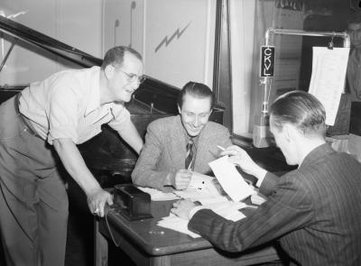 Les animateurs Jacques Normand et Roland Bayeur discutent avec le pianiste accompagnateur Billie Munroe dans un studio d'enregistrement de la station radio CKVL à Montréal.