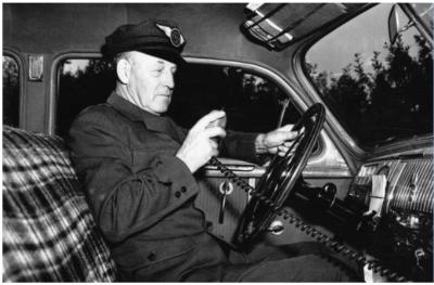 Photographie en noir et blanc montrant un chauffeur de taxi assis dans son véhicule.