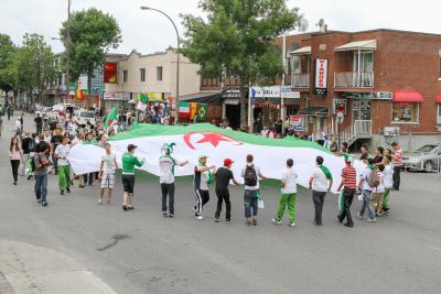 Une foule tenant un grand drapeau de l'Algérie dans le Petit Maghreb.