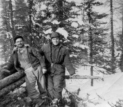 Photographie de deux hommes appuyés sur des billots de bois, dans la forêt en hiver.