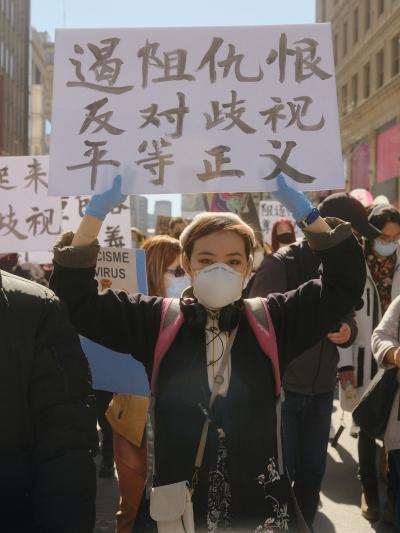 一群人在市中心路段上游行。图片正面，一位女孩将中文标语牌举过头顶。