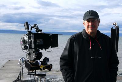 Denys Arcand avec sa caméra pose devant un cours d’eau
