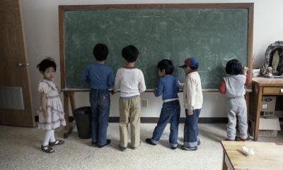 Six jeunes enfants dessinent à la craie sur un tableau dans une classe. 