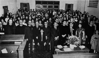 Photo en noir et blanc d’une foule debout à l'intérieur d’une église. Un jeune garçon se trouve devant la foule. 