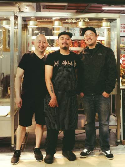 Photo couleur plein pied de trois hommes souriant posant debout devant un restaurant. 