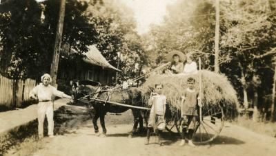 Un homme tenant un cheval qui tire une carriole de foin. Deux enfants posent devant et deux enfants sont assis sur le foin.