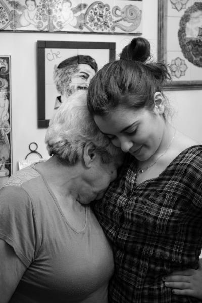 Photo en noir et blanc montrant une grand-mère et sa petite-fille enlacées en plan rapproché. Le visage de la grand-mère est caché dans l’épaule de sa petite-fille.