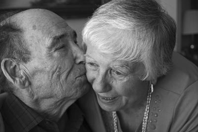 Photo en noir et blanc d’un homme âgé embrassant sa femme sur la joue en plan rapproché. .