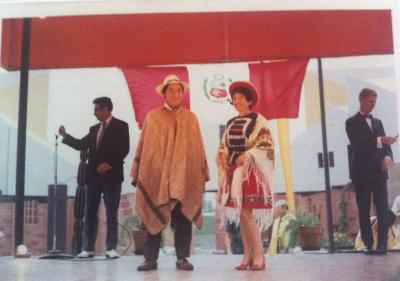 Un homme et une femme en habits traditionnels péruviens se tiennent sur une scène. En arrière-plan, deux hommes habillés d'un veston noir.