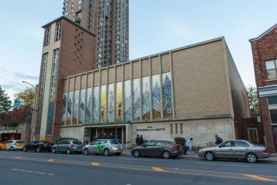  Photographie couleur de la façade d’une église. Sur la partie droite, il y a une mosaïque et, sur la partie gauche, sur la tour, une croix est visible.