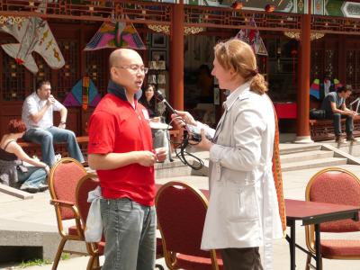 Une femme tenant un micro interviewe un homme d’origine chinoise sur une place publique dans le Quartier chinois.