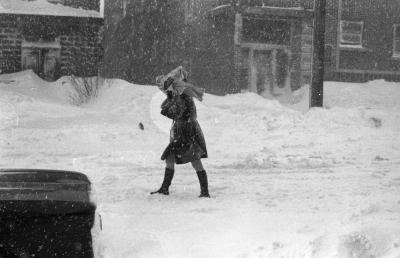 Une jeune femme tente de se protéger du vent et de la neige coiffée d’un journal