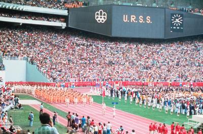 Photographie couleur de la délégation soviétique en orange paradant sur la piste du stade.