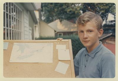 Garçon de 13 ans posant avec un tableau de liège avec une carte et autres cartons épinglés