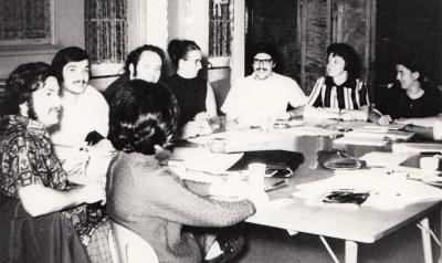 Quatre hommes et quatre femmes sont assis autour d’une table carrée sur laquelle se trouvent des feuilles de papier et des crayons.