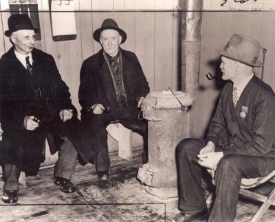 Trois hommes âgés assis autour d’un poêle