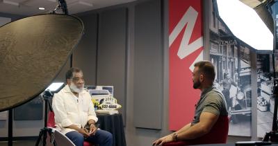 Photographie en couleur de deux hommes assis face à face en discussion dans un studio.