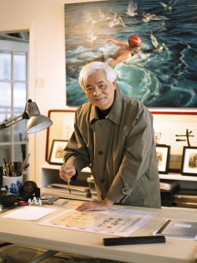 Photo couleur d’un artiste tenant un pinceau dans une main et l'autre main appuyée sur une table dans son atelier.