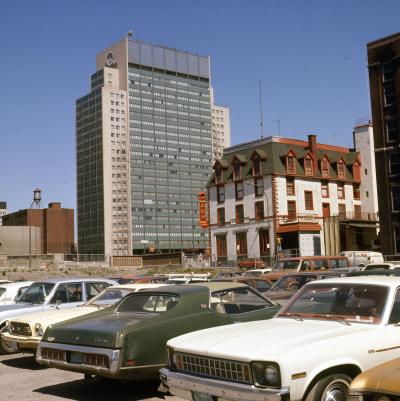 Photo couleur montrant un stationnement à l’avant-plan, un édifice abritant les Nouilles Wing au centre et un gratte-ciel à l’arrière-plan.