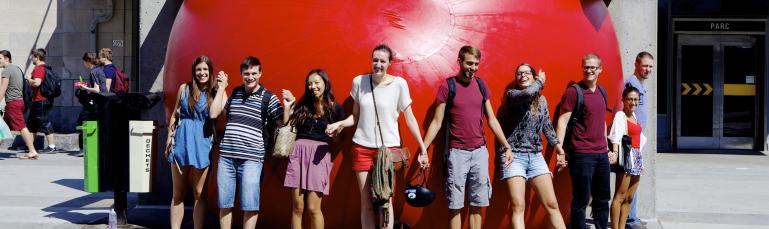 Neuf personnes se tiennent la main devant une grosse ballée gonflée orange devant une station de métro