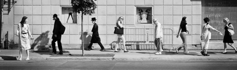 Photo en noir et blanc montrant une scène de rue : huit personnes circulent sur un trottoir du Mile End